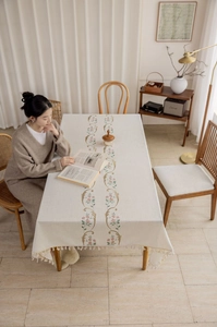 Close-up of pink flower embroidery and tassel edge on beige cotton linen tablecloth