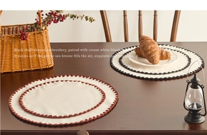 Detailed embroidery on round linen placemats with scalloped edges on a wooden table