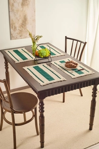 Detail of four-piece woven placemats with dark green stripes and fringed edges on wood table