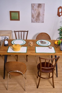 Detail of white linen placemats with green wavy embroidery on a rustic wooden table