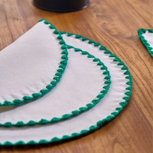 Round white fabric placemat with dark green crochet edges on a wooden table