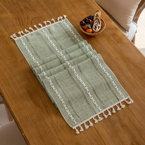 Moderner grasgrüner Tischläufer mit geometrischer Stickerei und Quasten auf Holztisch