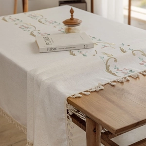Linen rectangle tablecloth with floral embroidery and tassel trim on wooden table
