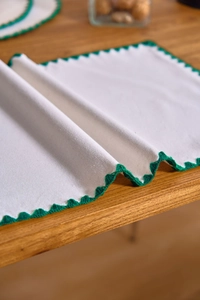 Close-up of white linen table runner with green scalloped crochet edge on wood table