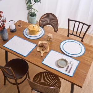 Modern white fabric placemat set with blue scalloped embroidery on a wooden table