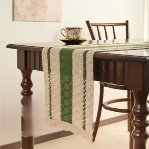 Close-up of dark green and beige knitted table runner with handmade tassels on wooden table