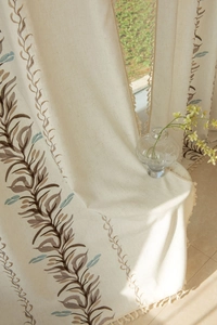 Detail of bohemian cream linen curtain featuring leaf embroidery and fringe edges