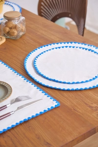 Detail of white cotton linen placemat with blue scalloped embroidery on wooden table
