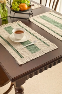 Detail of woven table mat featuring green stripes and fringe on a dark wood table