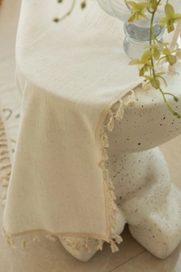 Close-up of cream cotton linen table runner featuring detailed bohemian tassel edges
