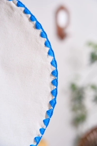 Detail of handcrafted round linen placemat featuring blue triangle edge embroidery