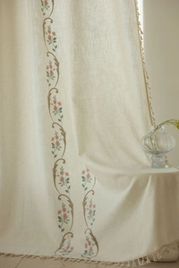 Detail of embroidered floral patterns and tassel fringe on linen-textured curtains