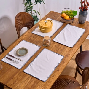 Set of 4 cream embroidered round placemats with navy wavy edges on wood dining table