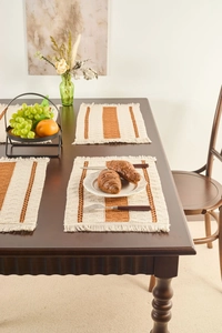 Detail of Nordic woven placemat with brown stripes and tassels on dark wood table