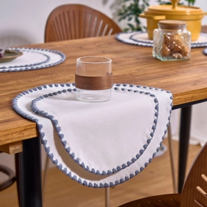 White embroidered round placemat with blue scalloped edges on a wooden dining table
