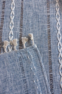 Detail eines hellblauen Tischläufers mit hohlen Quasten und geometrischer Stickerei