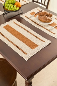 Close-up of woven rectangular placemat with red stripes and fringe on a wooden table