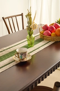 Detail of green and white striped woven table runner with boho tassels on wood table