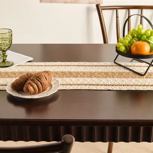 Close-up of woven table runner with tassels on a wooden table with dining accessories