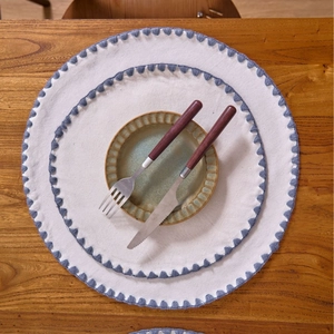 Detail of round cotton linen placemats with blue embroidered edges on a wooden table