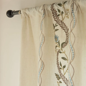 Detail view of beige linen-textured curtain with delicate floral embroidery on black rod