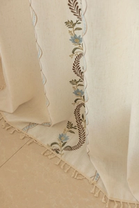 Detail of embroidered floral patterns and tassel fringe on beige cotton linen curtains