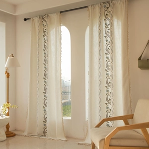 Detail of beige cotton linen curtains with blue floral embroidery and fringe tassels