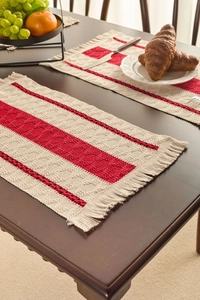 Detail view of woven striped table mat with red tassels on a wooden dining table