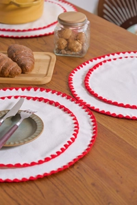 Close-up of round white cotton linen placemat with red scalloped crochet edge on wood table
