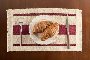 Macro detail of Nordic woven placemat with wine red stripes and tassels on wooden table