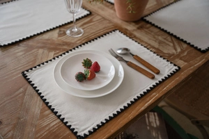 Close-up of beige linen placemat with black zigzag embroidery on a wooden dining table