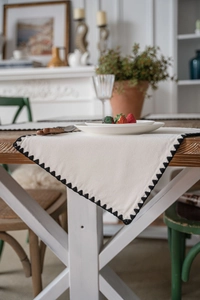 Detail of off-white cotton linen placemat with black crochet triangular edge on wood table