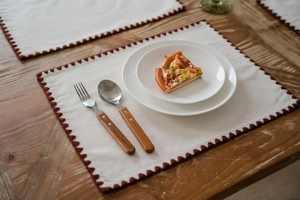 Detail of white cotton linen placemat with red wavy embroidered edges on wooden table