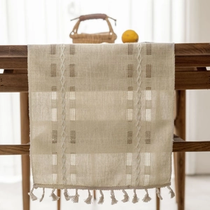 Neutral beige woven table runner with hollow mesh design and tassel trim on wooden table