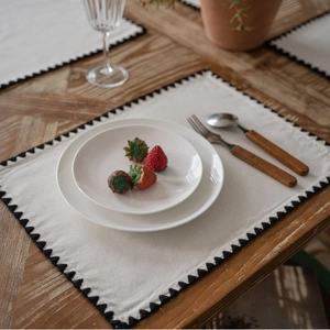 Minimalist cotton linen placemat with black stitched edges on a rustic wooden table