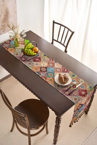 Detail of bohemian orange geometric table runner featuring brown tassel ball trim ornaments