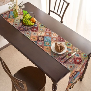 Bohemian geometric table runner with orange diamond patterns and tassels on wood table