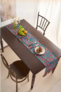 Detail of red cherry jacquard table runner with colorful tassels on dark blue fabric
