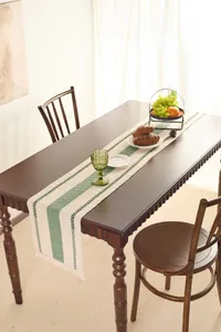 Detail of woven linen table runner with green stripes and tassels on wood table