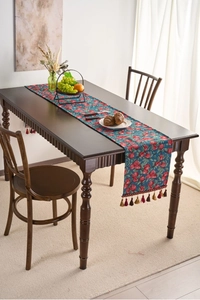 Detail of red cherry jacquard table runner with colorful tassels on dark wood table