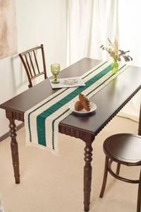 Close-up of cream woven table runner with green stripes and decorative tassels on wood