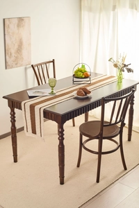Detail of minimalist khaki woven table runner with brown stripes on dark wood table