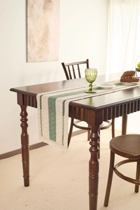 Detail of woven table runner with green stripes and tassels on a dark wood table