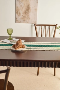 Macro shot of dark green cable-knit table runner with elegant tassels on a wooden table