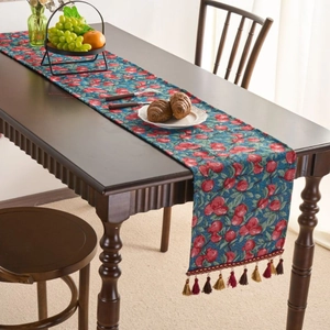 Floral table runner with red fruit patterns and colorful tassels on dark wood table