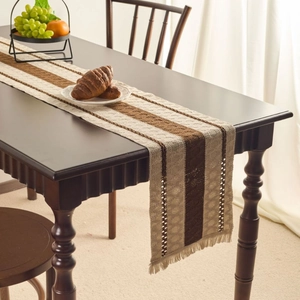 Nordic khaki striped table runner with woven texture and fringe on a dark wooden table