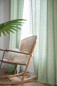 Detailed embroidery of white floral patterns on sage green semi-sheer linen curtains