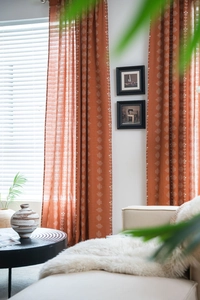 Détail du rideau terre cuite semi-transparent aux motifs géométriques et végétaux blancs