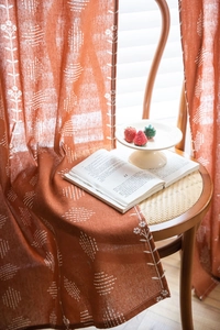 Détail du rideau semi-occultant à fleurs orange drapé sur une chaise en bois