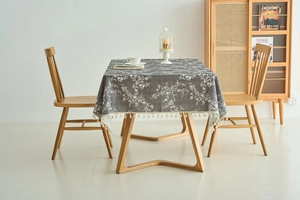 Close-up of grey rectangular tablecloth with white floral pattern and cream tassel fringe